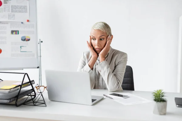 Choqué femme d'affaires senior regardant ordinateur portable sur le bureau — Photo de stock