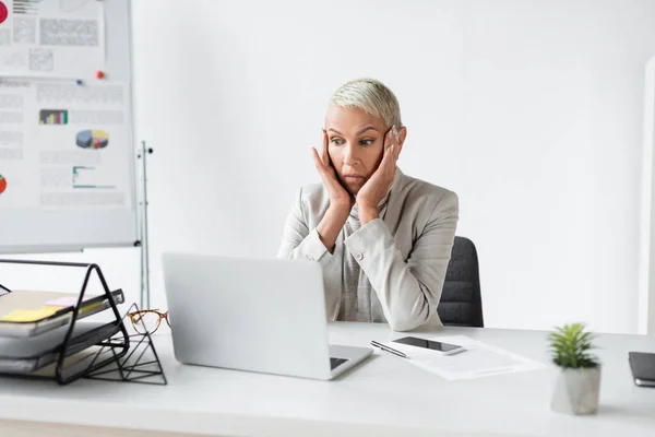 Geschockte Seniorin blickt auf Laptop auf Schreibtisch — Stockfoto