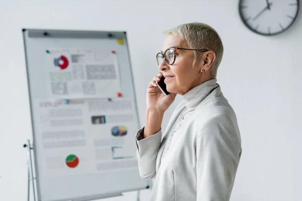 Donna d'affari sorridente con i capelli grigi che parla sul telefono cellulare in ufficio — Foto stock