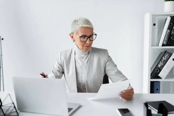 Empresária sênior em óculos olhando para o documento no escritório — Fotografia de Stock