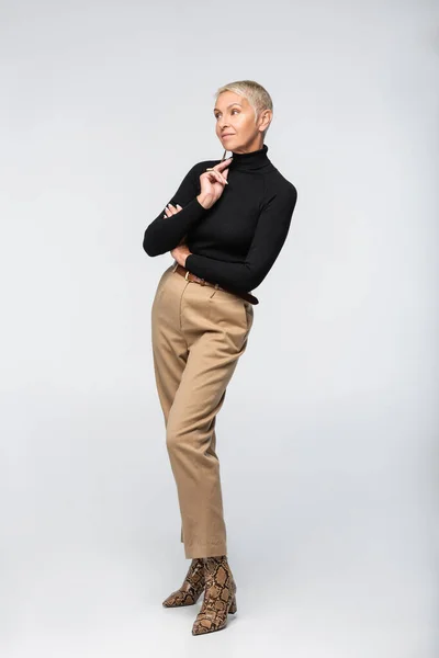 Stilvolle Seniorin in beiger Hose und Rollkragen posiert auf grau — Stockfoto