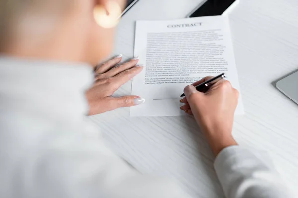 Empresária desfocada assinando documento perto do smartphone na mesa — Fotografia de Stock