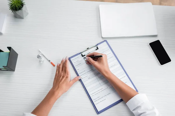 Vista superior de la prescripción de la escritura del médico cerca de gadgets en el escritorio - foto de stock