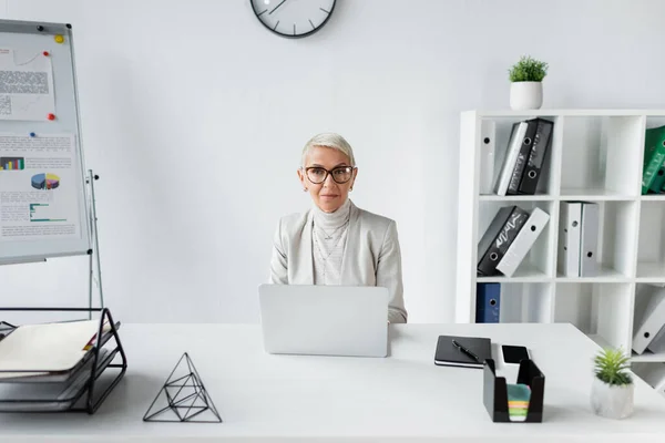 Seniorin mit Brille blickt in modernes Büro in die Kamera — Stockfoto