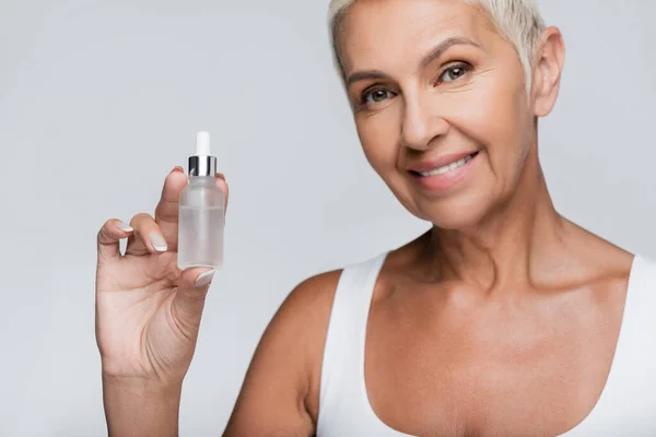 Heureuse femme âgée tenant bouteille avec sérum isolé sur gris — Photo de stock