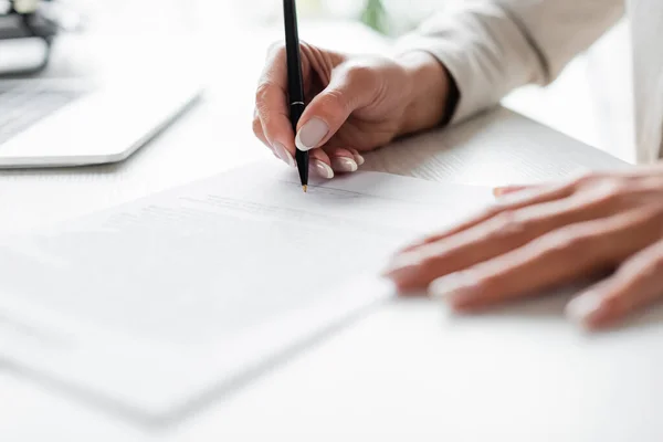 Cropped view of businesswoman signing blurred document — Stock Photo