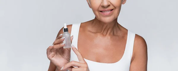 Cropped view of happy senior woman holding bottle with serum isolated on grey, banner — Stock Photo