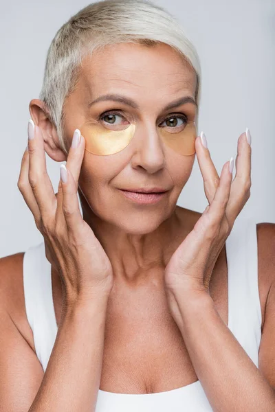 Retrato de mujer mayor aplicando parches oculares de colágeno aislados en gris - foto de stock