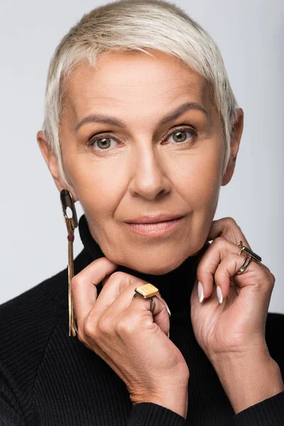 Retrato de mujer mayor con arete largo y cuello alto negro aislado en gris - foto de stock