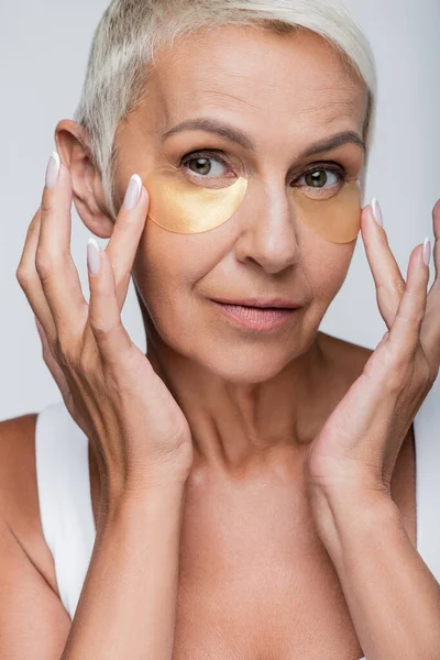 Portrait of senior woman applying eye patches isolated on grey — Stock Photo