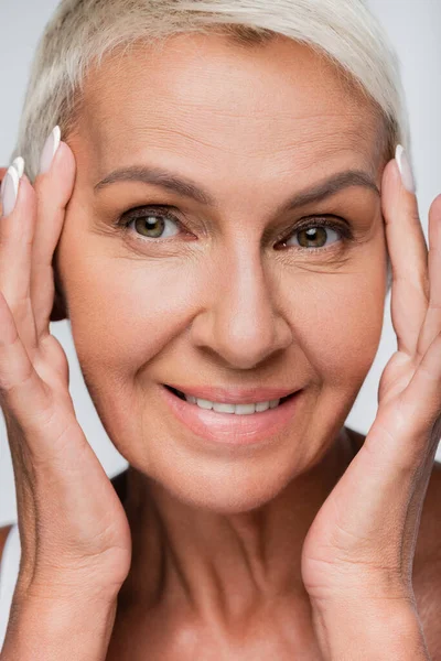 Porträt einer Seniorin, die ihr Gesicht berührt, während sie isoliert auf grau lächelt — Stockfoto