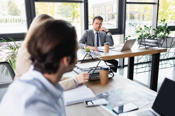 Jeunes gens d'affaires travaillant dans le bureau près des appareils et des documents sur les bureaux, au premier plan flou — Photo de stock