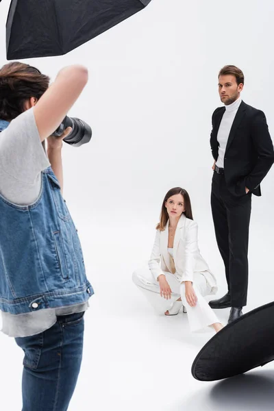 Young models in black and white suits posing near photographer on white — Stock Photo
