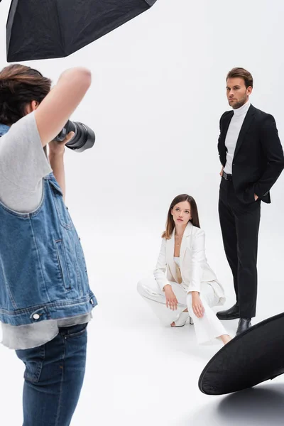 Modelos jóvenes en trajes blancos y negros posando cerca de fotógrafo en blanco - foto de stock