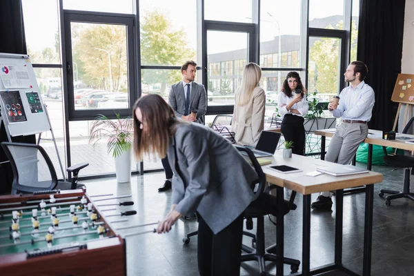 Pessoas de negócios falando durante coffee break no escritório moderno perto de mulher borrada jogando futebol de mesa — Fotografia de Stock