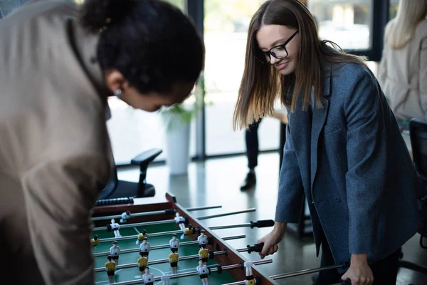 Donna d'affari sorridente che gioca a calcio balilla con un collega afroamericano offuscato — Foto stock