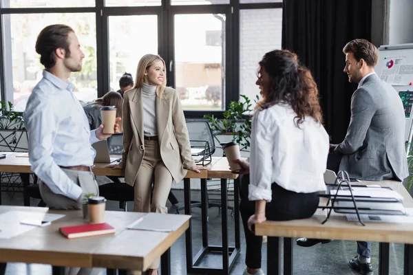 Young multiethnic business colleagues with coffee to go talking in office — Stock Photo