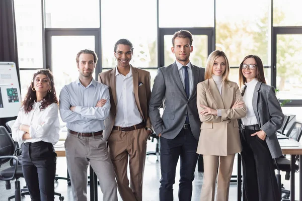 Gente de negocios multiétnicos en ropa formal sonriendo a la cámara mientras está de pie en la oficina - foto de stock