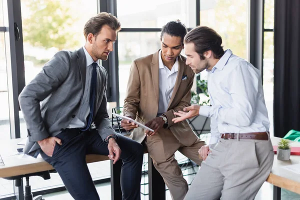 African american businessman showing digital tablet during conversation with colleagues in office — Stock Photo