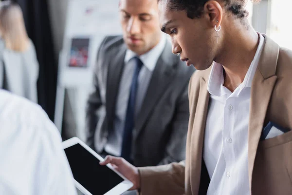 Joven empresario afroamericano sosteniendo tableta digital con pantalla en blanco cerca de colegas borrosos - foto de stock