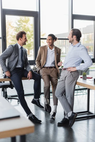 Hombre de negocios afroamericano positivo gesticulando mientras habla con colegas en el cargo - foto de stock