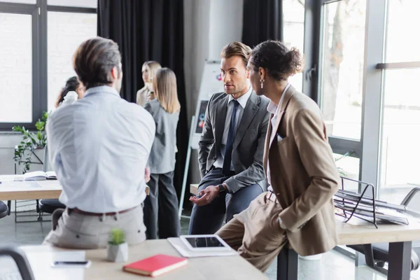 Молоді багатонаціональні бізнесмени розмовляють в офісі біля розмитих бізнесменів — стокове фото