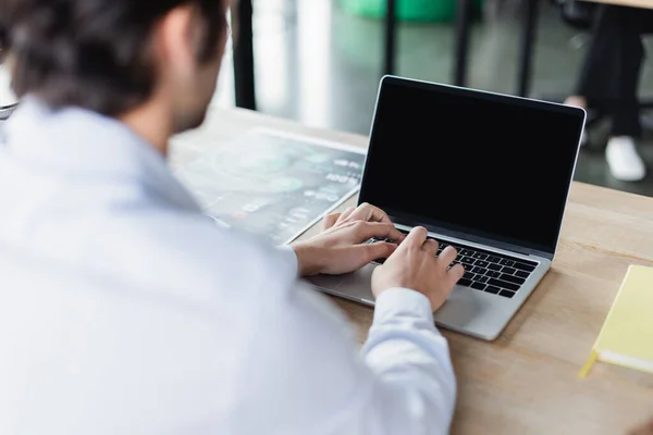 Partial view of blurred businessman typing on laptop with blank screen — Stock Photo