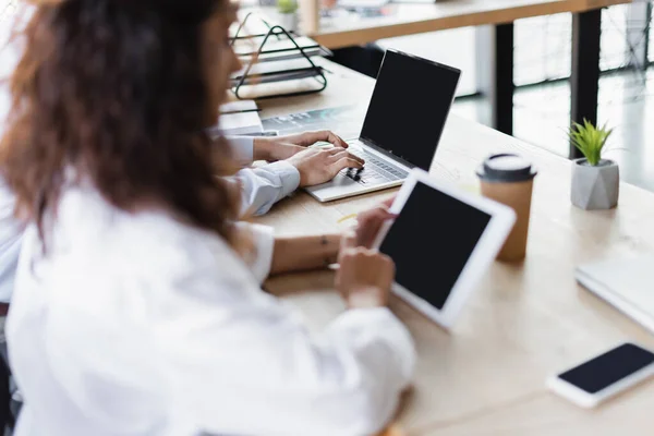 Blurred businesswoman holding digital tablet with blank screen near colleague typing on laptop — Fotografia de Stock