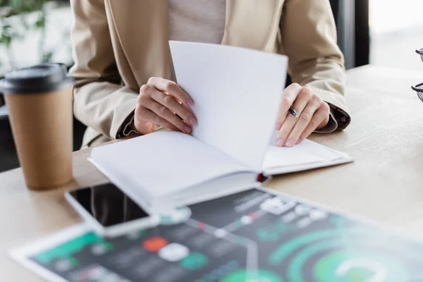 Vista recortada de la mujer de negocios sentada en el lugar de trabajo cerca de portátil vacío y teléfono móvil con pantalla en blanco - foto de stock