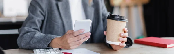 Abgeschnittene Ansicht einer Geschäftsfrau, die Pappbecher hält, während sie ihr Handy im Büro benutzt, Banner — Stockfoto