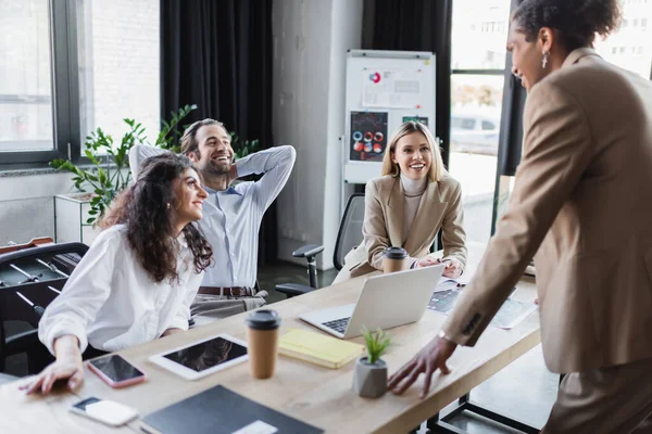 Junger afrikanisch-amerikanischer Geschäftsmann im Gespräch mit aufgeregten Kollegen am Schreibtisch im Büro — Stockfoto