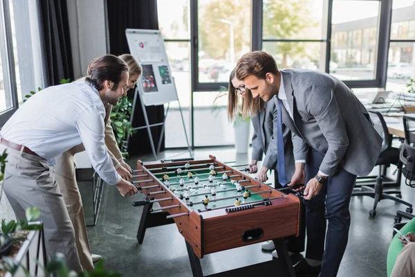 Young and happy business people in formal wear playing table football in office — Stock Photo