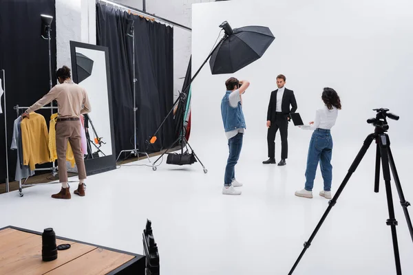 Equipe multiétnica trabalhando durante sessão de fotos com modelo moderno em estúdio — Fotografia de Stock