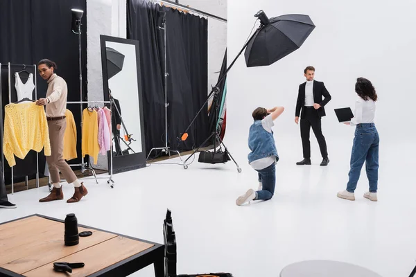Uomo in abito nero in posa durante la sessione fotografica vicino squadra multiculturale — Foto stock