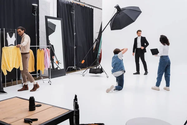 Mann im schwarzen Anzug posiert bei Fotosession in der Nähe multikulturellen Teams — Stockfoto