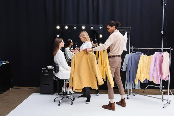 Joven artista de maquillaje y estilista afroamericano preparando modelo profesional en estudio de fotografía - foto de stock