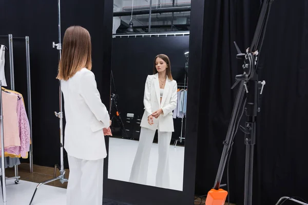 Modelo profissional no terno elegante branco que está perto do espelho no camarim — Fotografia de Stock