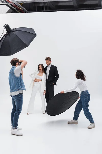 Modèles élégants posant près photographe et assistant avec réflecteur dans le studio photo — Photo de stock