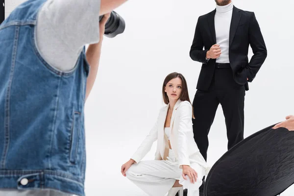 Blurred photographer taking photo of models in stylish suits on white — Stock Photo