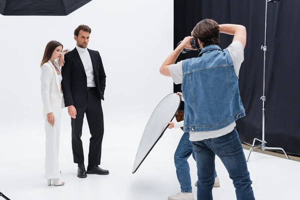 Modelos jovens e elegantes posando perto de fotógrafo e assistente no estúdio de fotografia — Fotografia de Stock