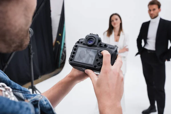 Professional photographer looking at viewfinder of digital camera near blurred models in photo studio — Stock Photo