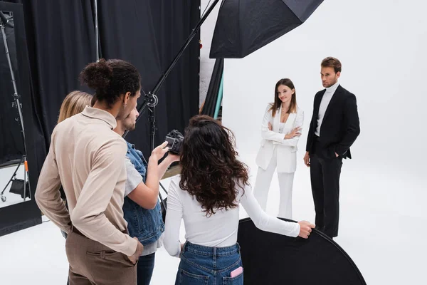 Fotograf mit multiethnischen Kollegen, die Digitalkameras in der Nähe junger und trendiger Modelle betrachten — Stockfoto