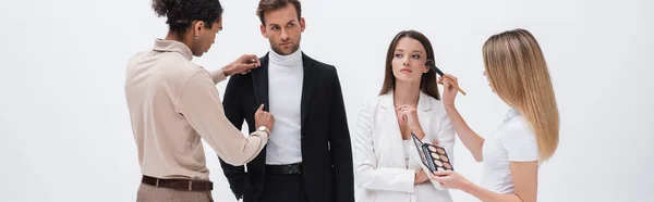 Young interracial stylist and makeup artist preparing professional models to photo session isolated on white, banner — Stock Photo