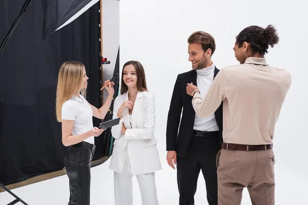 African american stylist and blonde makeup artist preparing cheerful models in photo studio — Stock Photo