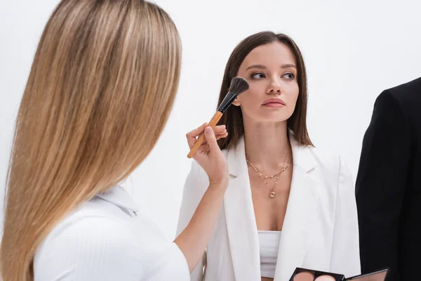 Rubia maquillaje artista aplicando maquillaje en joven morena modelo aislado en blanco - foto de stock