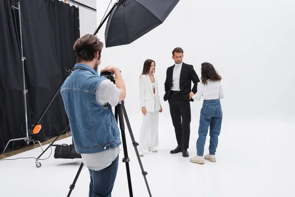 Photographe ajuster appareil photo numérique tandis que le directeur artistique parler avec des modèles en studio photo — Photo de stock