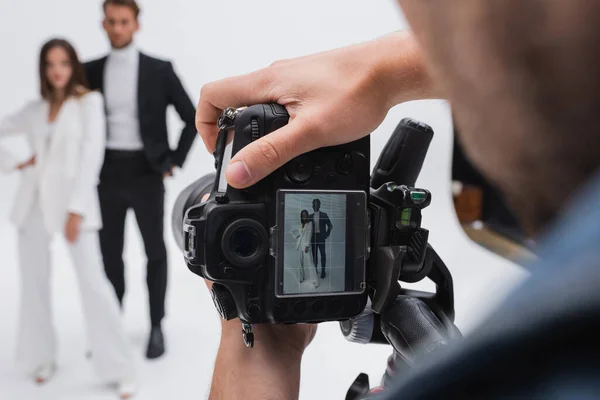 Selective focus of digital camera in hands of photographer near blurred models on white — Fotografia de Stock