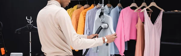 Cropped view of african american stylist using steamer while cleaning clothes in dressing room, banner — Stock Photo