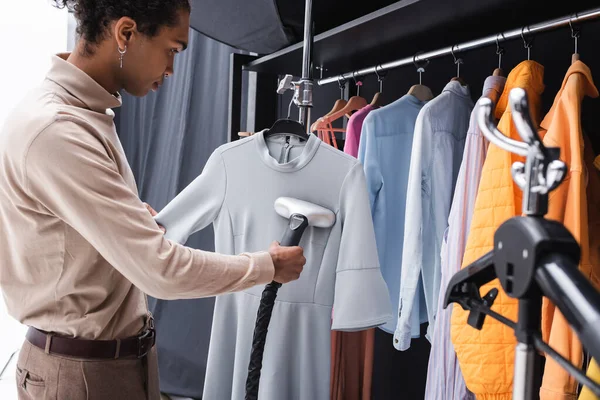 African american stylist cleaning dress with steamer in dressing room — Stock Photo