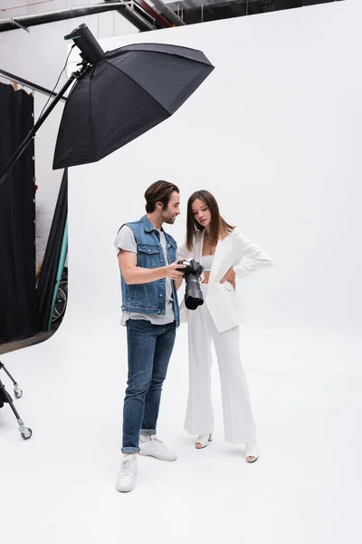 Young model looking at digital camera in hands of photographer in photo studio — Foto stock